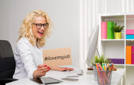 Woman at desk holding sign that says "I love my job."