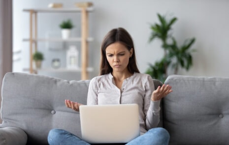Content personalization - Woman looking at laptop with a confused expression and her hands up in the air--she is displeased with what she sees on laptop.