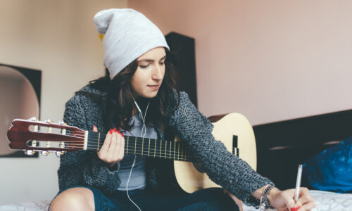 Woman writing song with guitar and paper